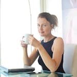 Young woman sitting at her desk, holding a coffee cup and smiling. Ideal for workplace and lifestyle themes.